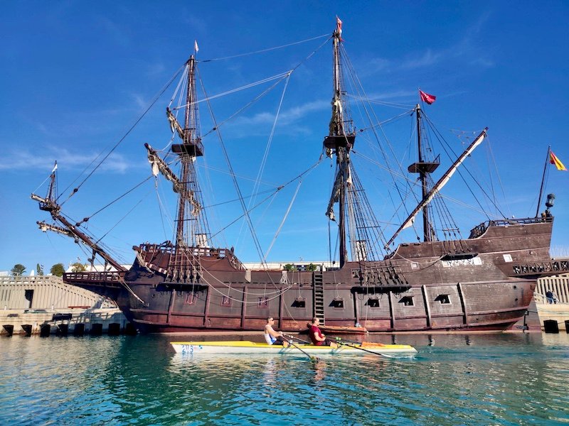 Foto remando en el doble de remo de mar con David Casinos, pasando por delante del Buque Nueva Andalucia