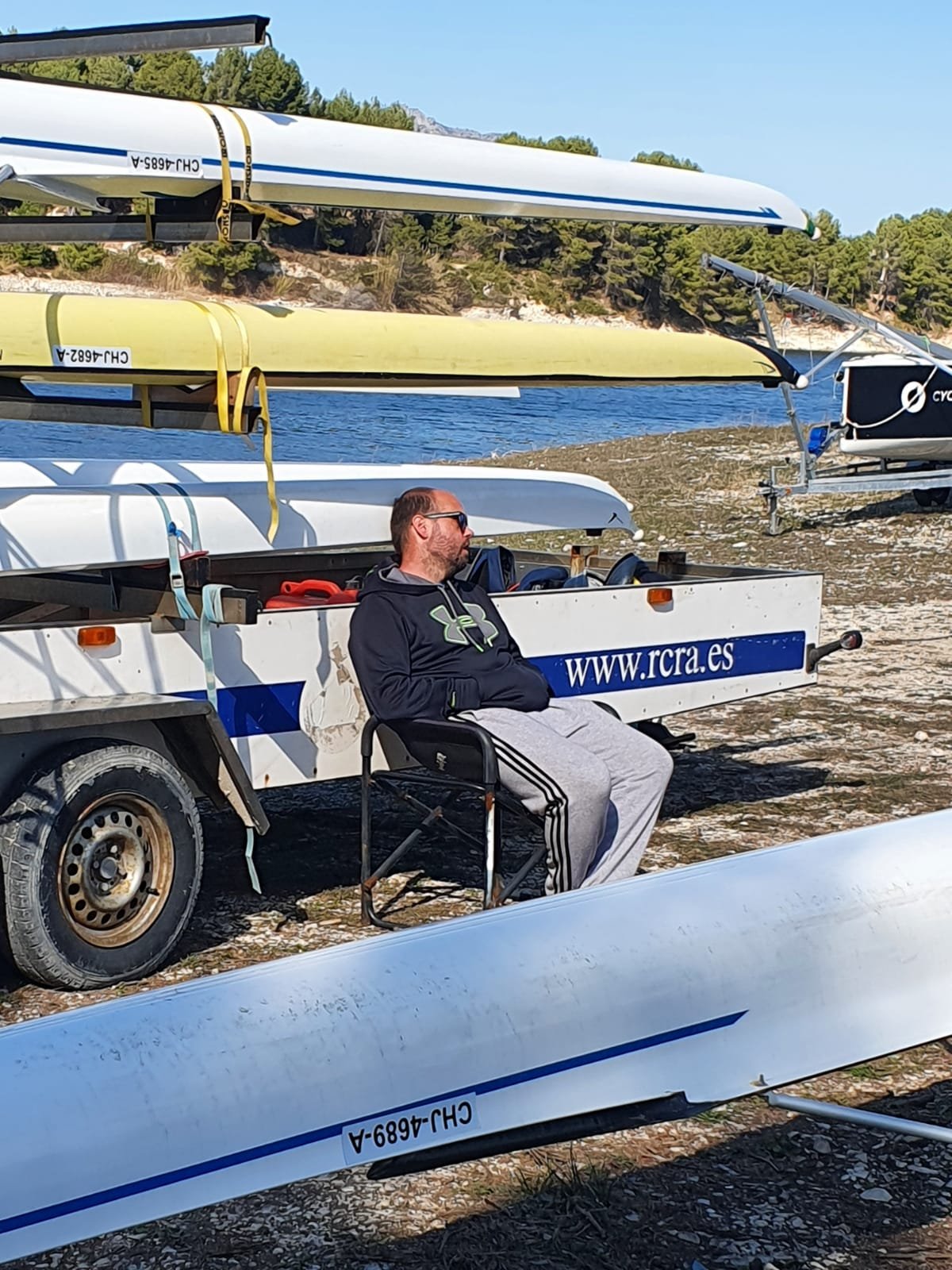 Foto sentado en una silla junto al remorque de los botes de remo cuidándolos